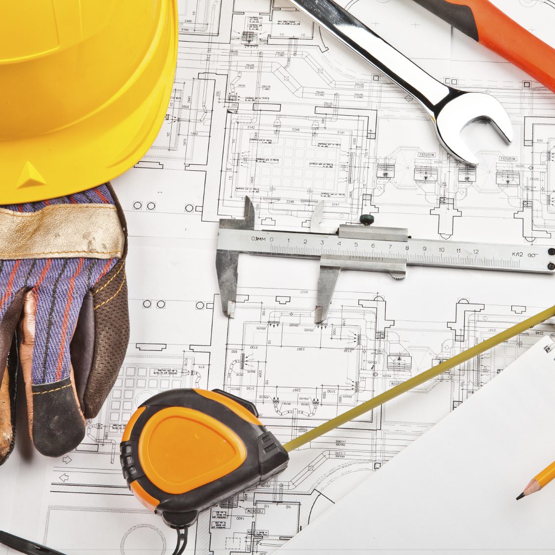 Construction tools and plans with a hard hat and gloves on a work surface.