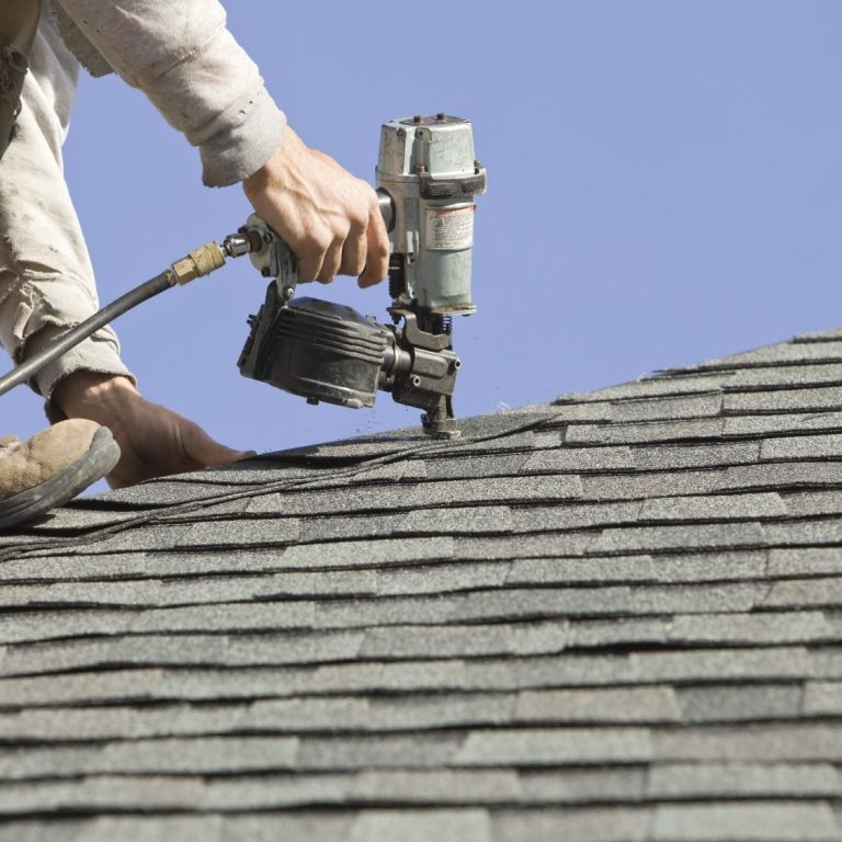 A person using a nail gun to install shingles on a sloped roof.