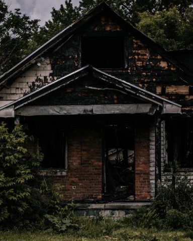 Dilapidated house with burnt exterior and overgrown vegetation.
