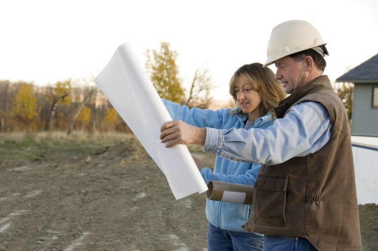Two construction workers review blueprints outdoors at a building site.