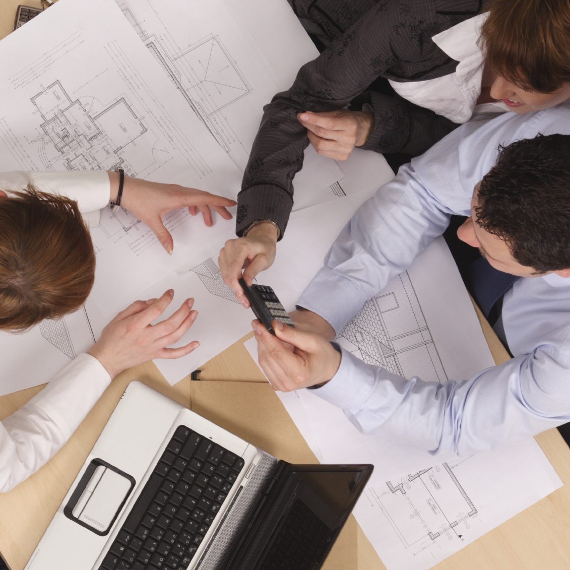 Four people collaborated over blueprints and a laptop on a table.