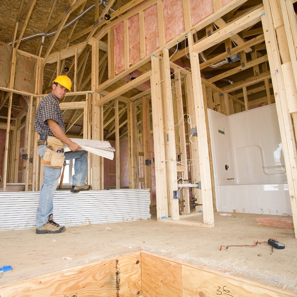 Construction worker reviewing blueprint plans in a partially framed interior space.