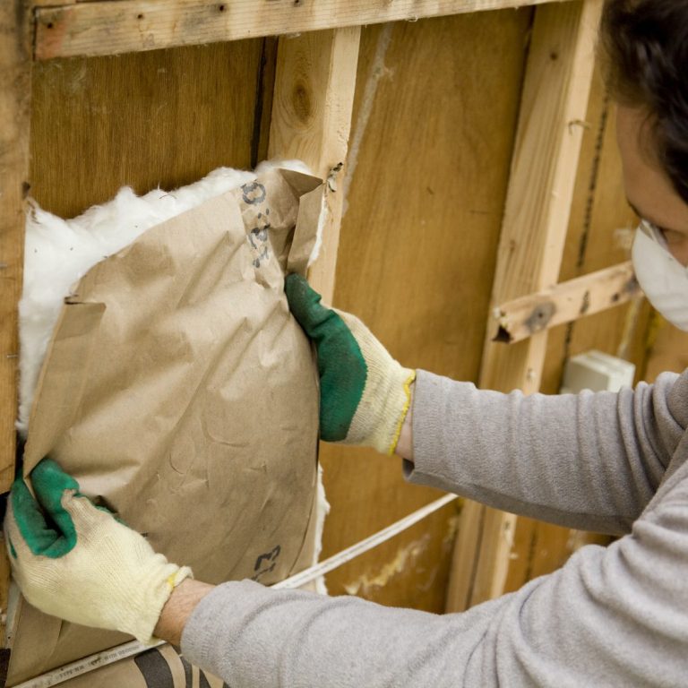 A person wearing gloves installing insulation in a wall cavity.
